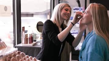 A makeup artist applying makeup to a client in a well-lit room with various cosmetic products on display.