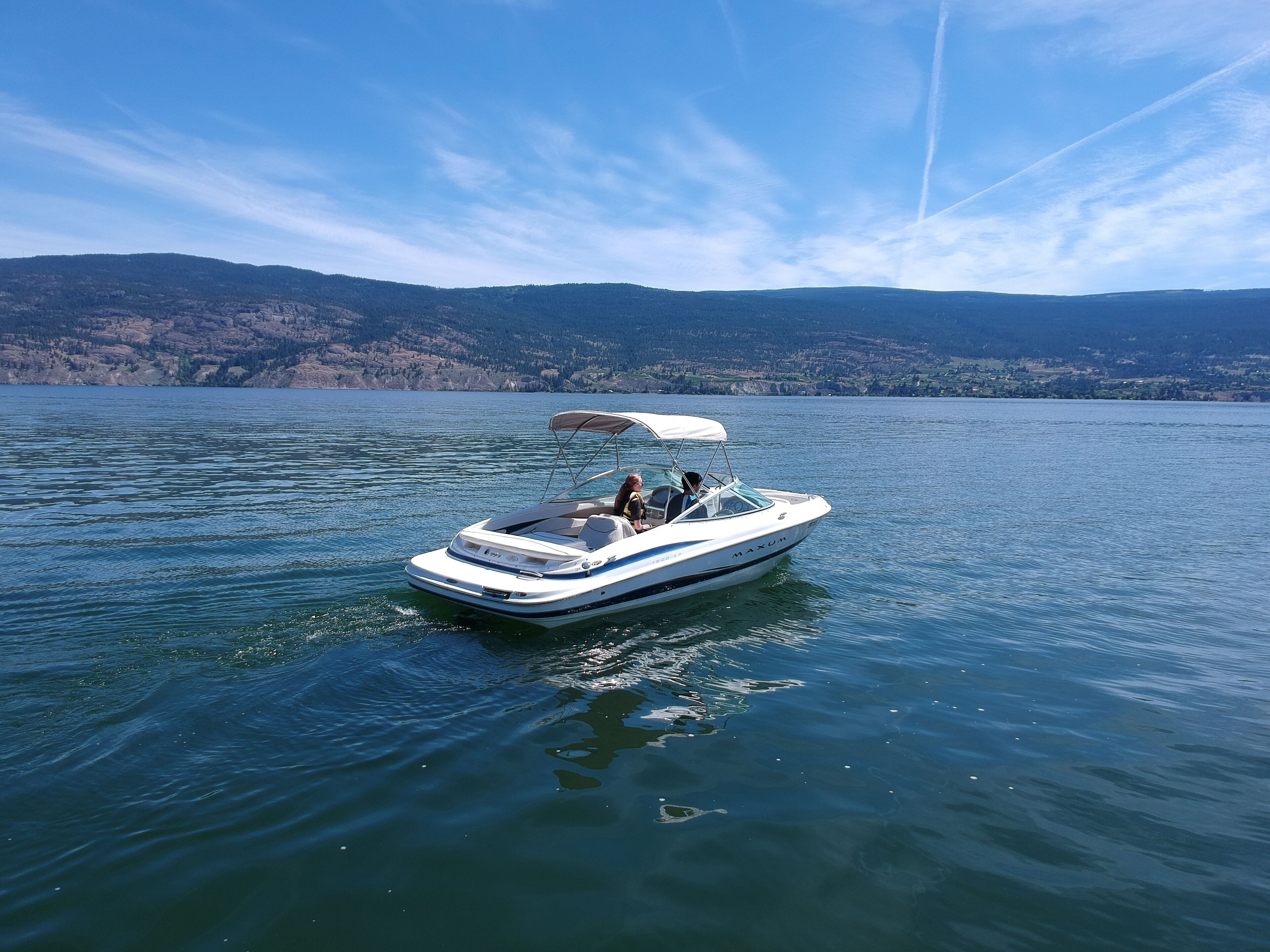 A small, white motorboat with a canopy on a calm lake.