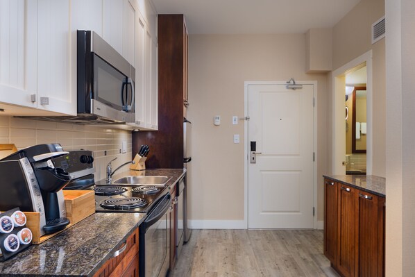 Una cocina compacta con microondas, estufa, cafetera y armarios de madera.