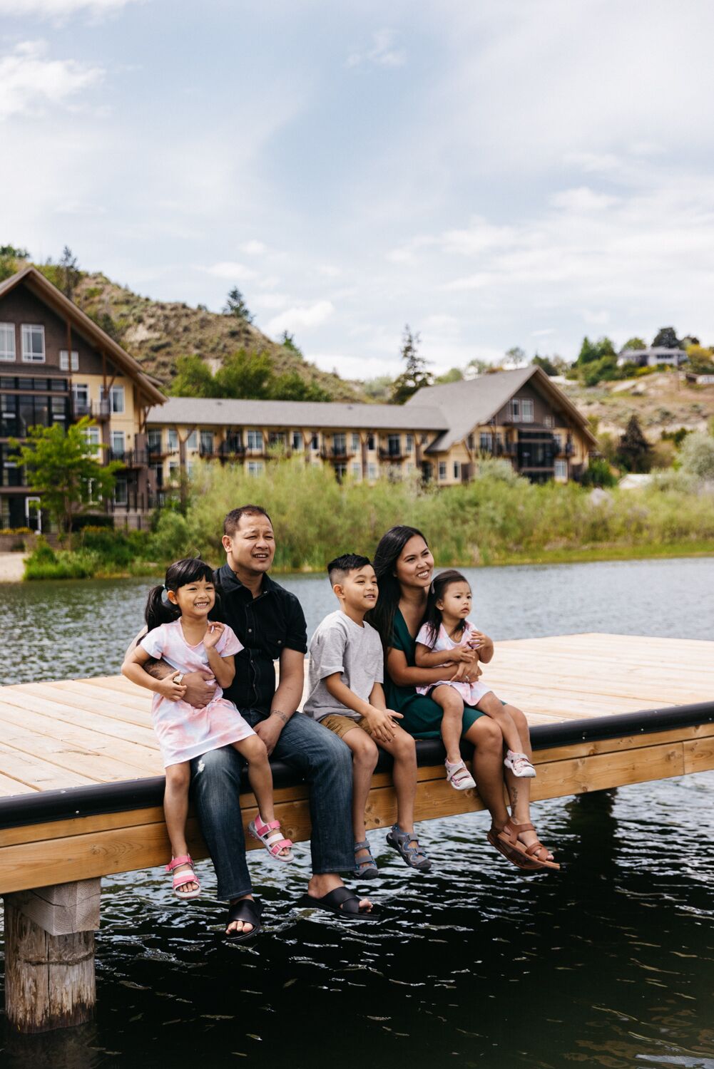 A family on a wooden dock by a lake with houses in the background.