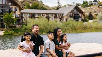 A family on a wooden dock by a lake with houses in the background.