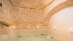 Habitación de paredes de piedra con una bañera, velas y un banco de madera.