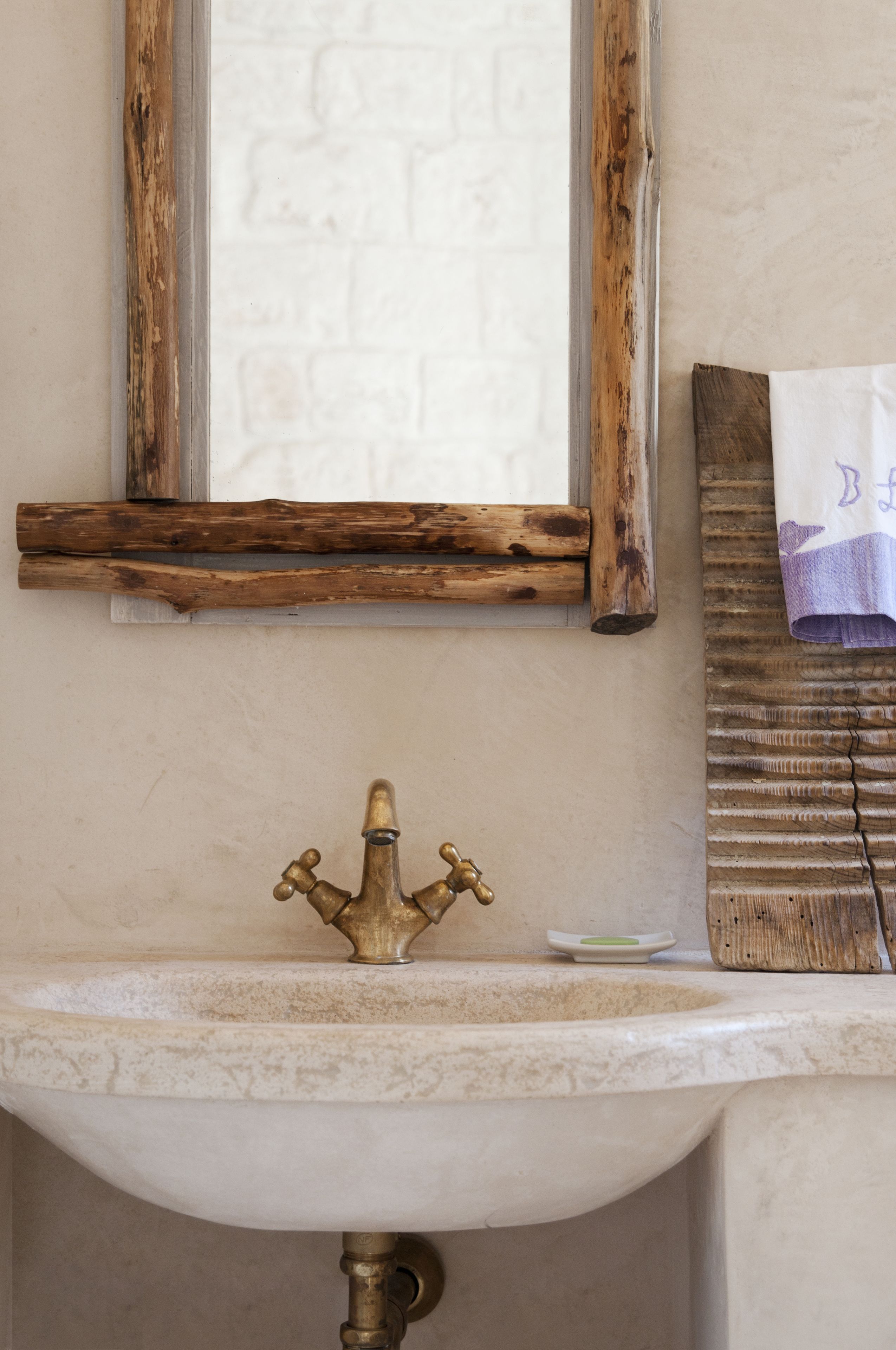 A bathroom with a rustic wooden-framed mirror, a vintage brass faucet, and a wooden towel rack.