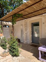 A covered outdoor area with a door marked '10', a wicker chair, and a small potted plant.