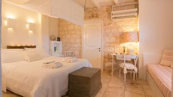 A bedroom with a large bed, a chest of drawers, a small table with a chair, and a wall-mounted air conditioner.