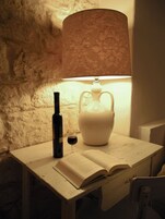 A table with a wine bottle, a glass of wine, and an open book under a lamp.
