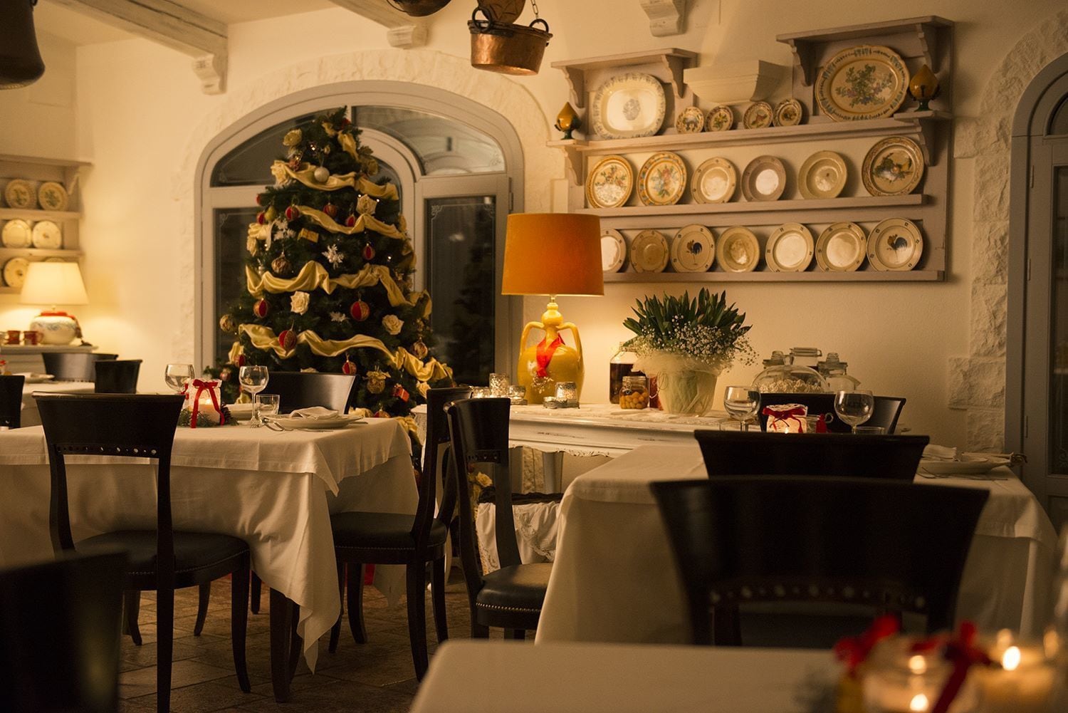 Un comedor con un árbol de Navidad, mesas dispuestas para comer y una pared decorada con platos.