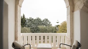 A balcony with two chairs and a table, overlooking a garden with trees and a white railing.