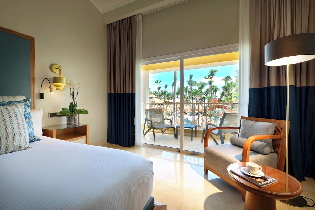 Habitación de hotel con cama, una silla, una mesa con una taza, una planta y vistas al exterior.