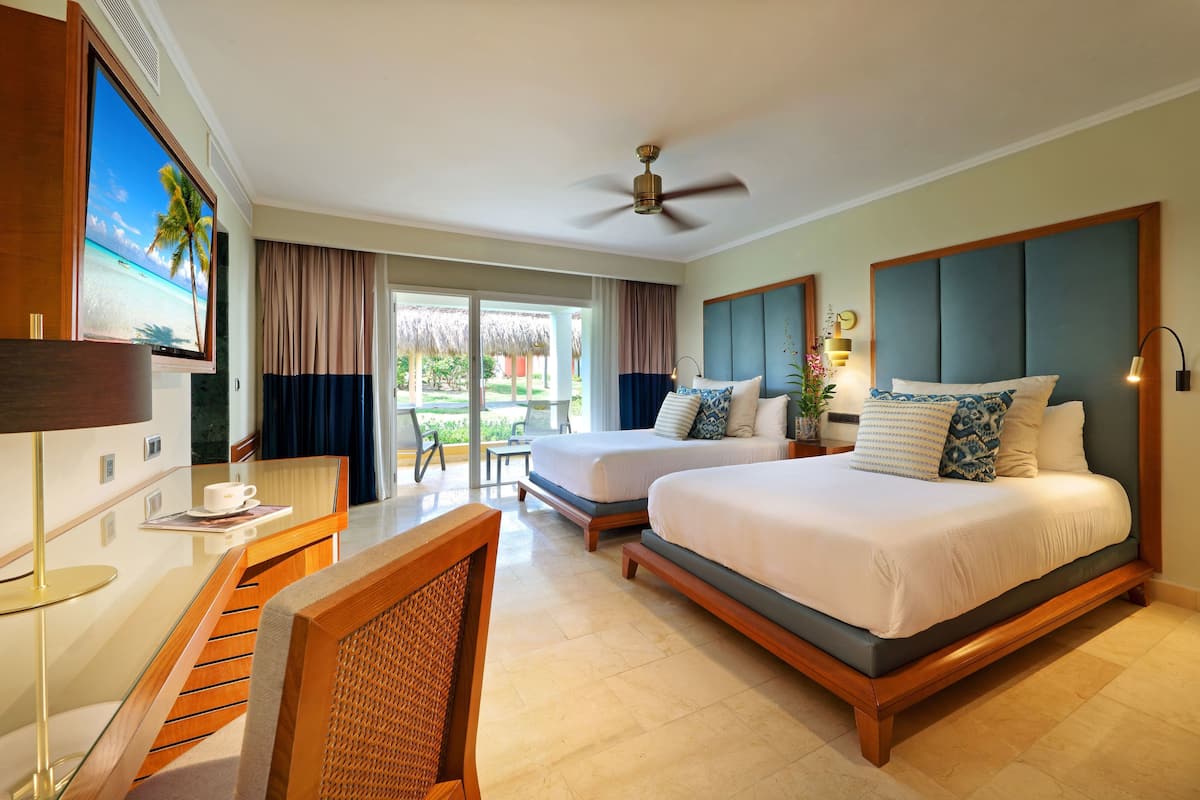 A hotel room with two beds, a desk, a TV, and a ceiling fan.