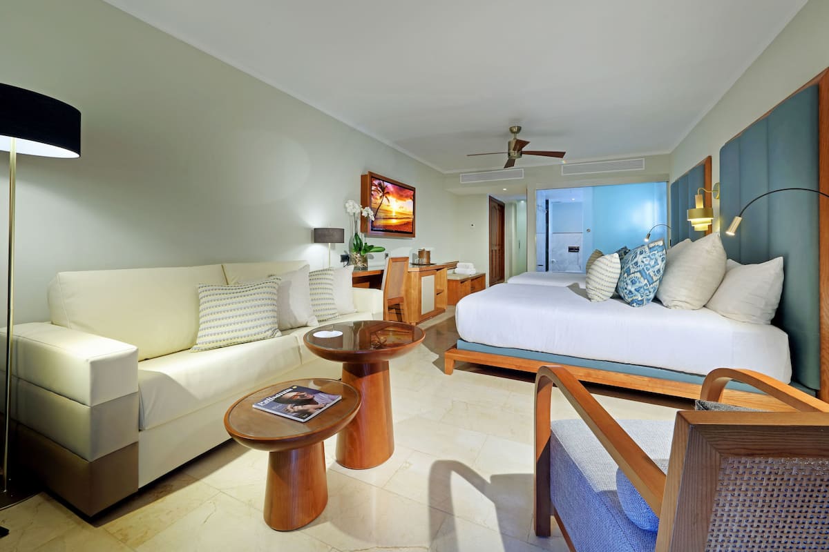 A modern hotel room with a sofa, a bed, a coffee table, and a desk.
