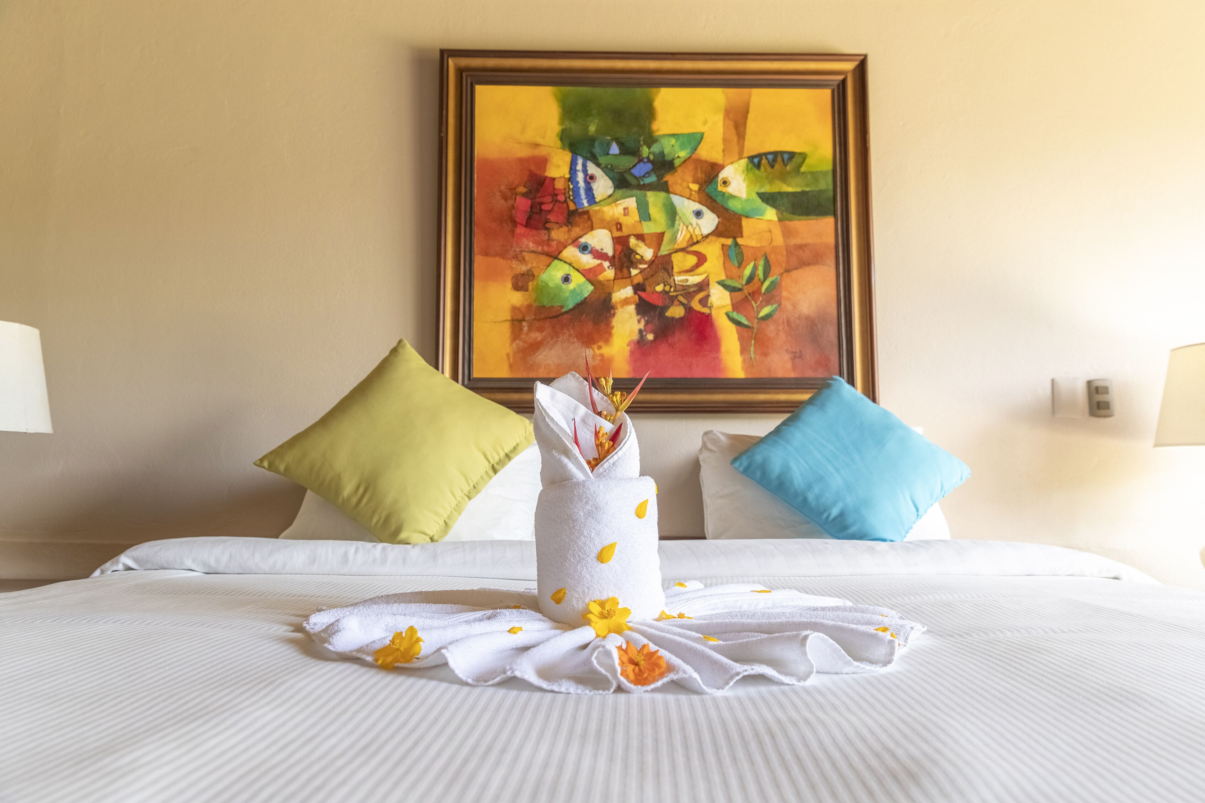 A neatly made bed with white linens, a towel with flowers, and two pillows in different colors.