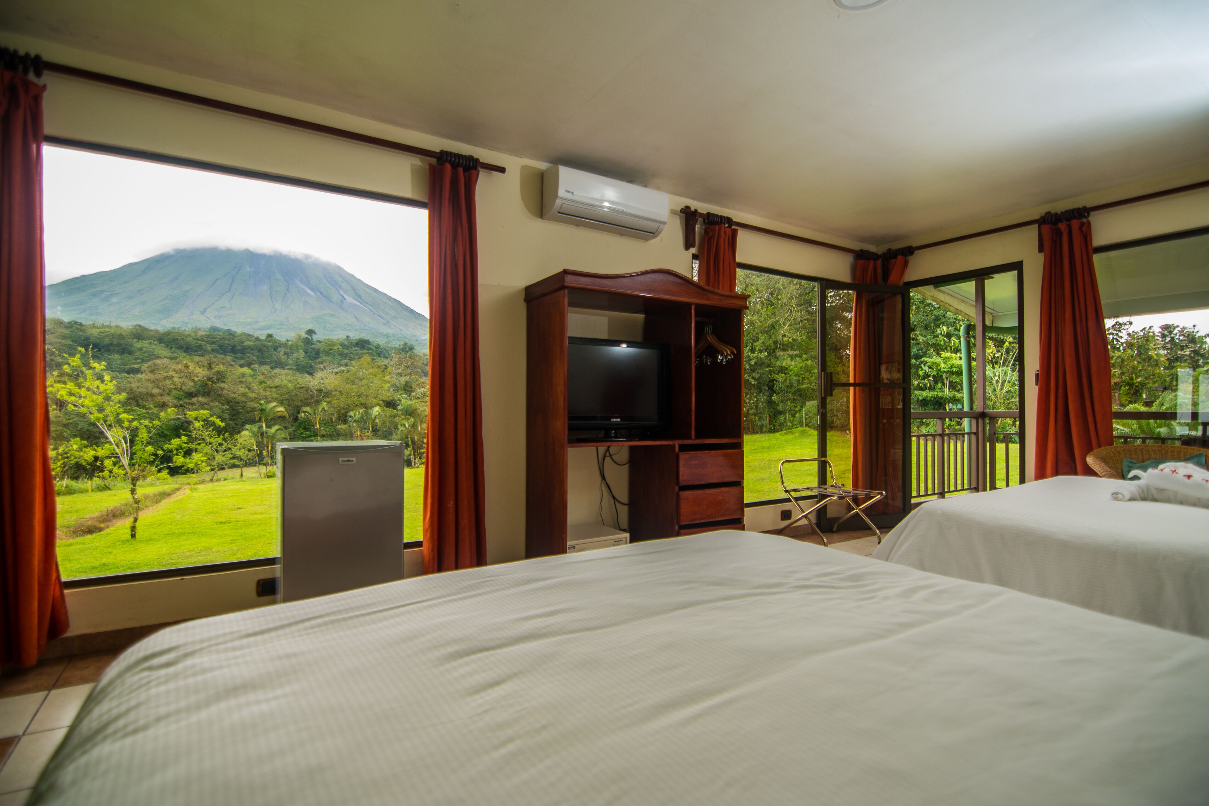 A hotel room with two beds, a TV, and a view of a mountain.