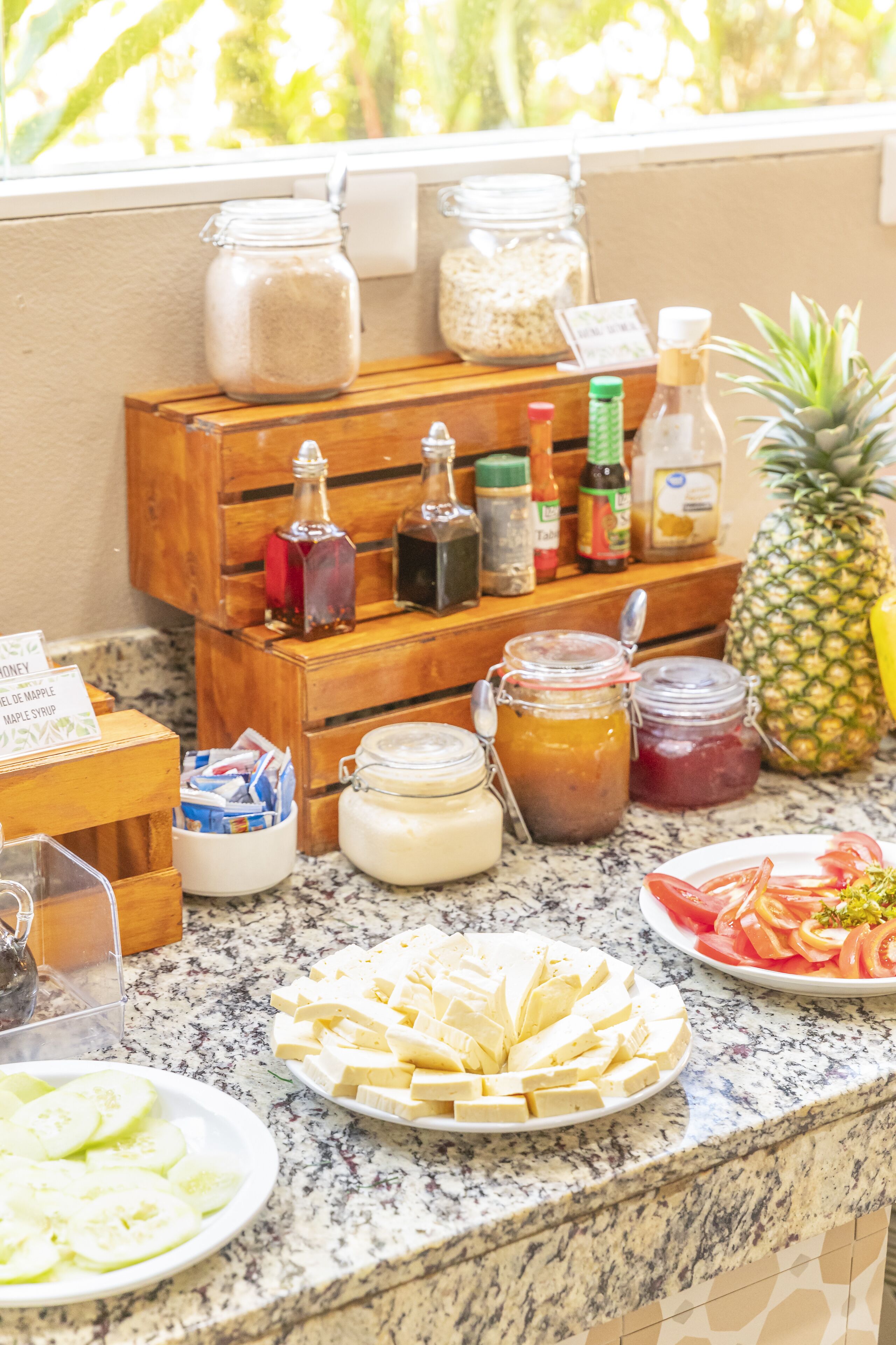 A kitchen counter with various food items and condiments, including jars of honey, maple syrup, and other spreads, as well as plates of sliced fruit and cheese.
