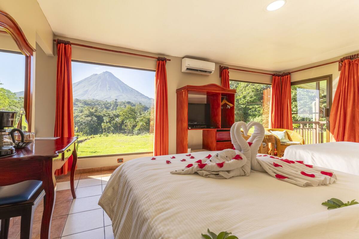Een hotelkamer met een bed, bureau, televisie en uitzicht op een berg.