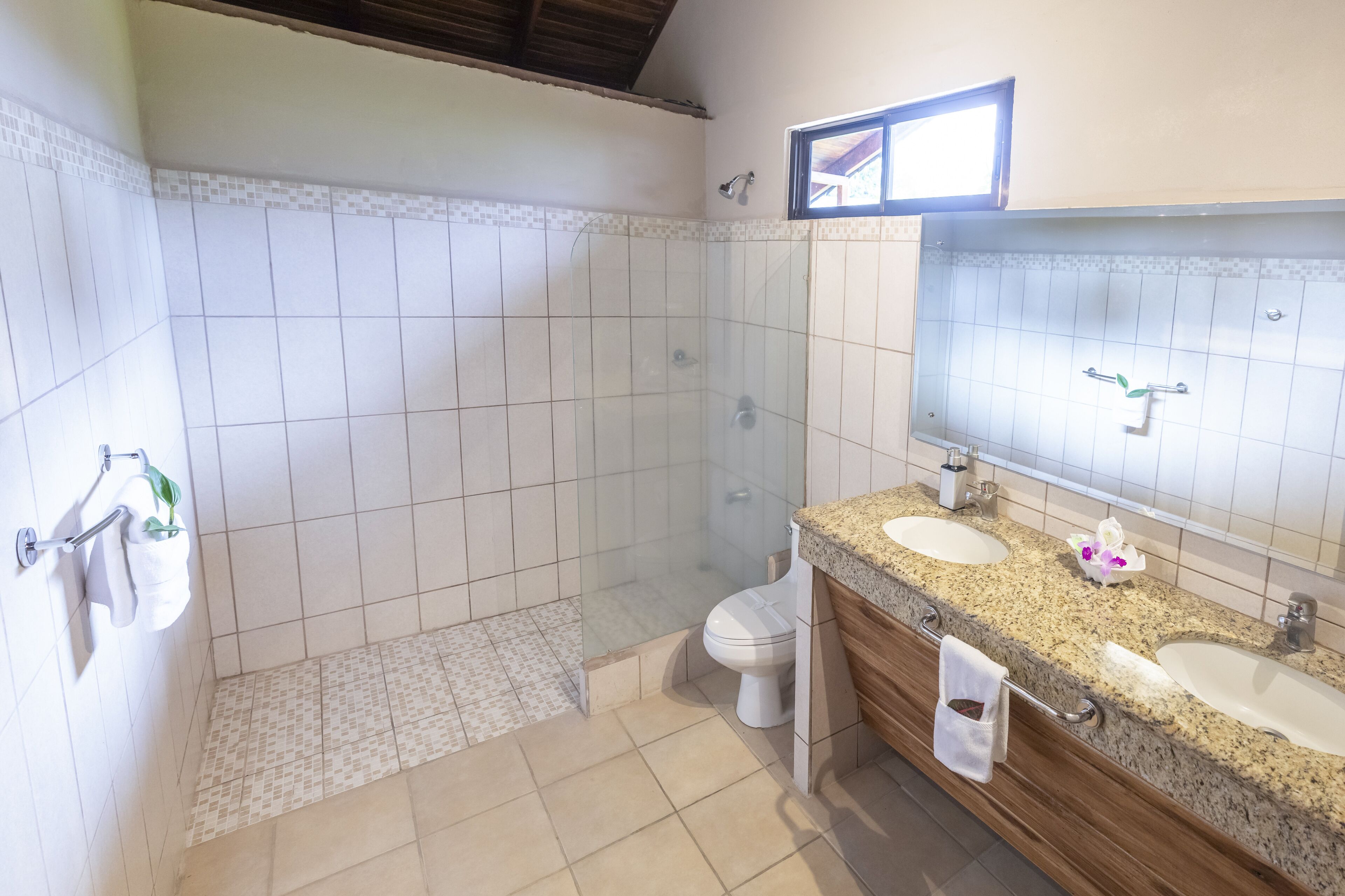 Un baño con dos lavamanos, inodoro, ducha y espejo.