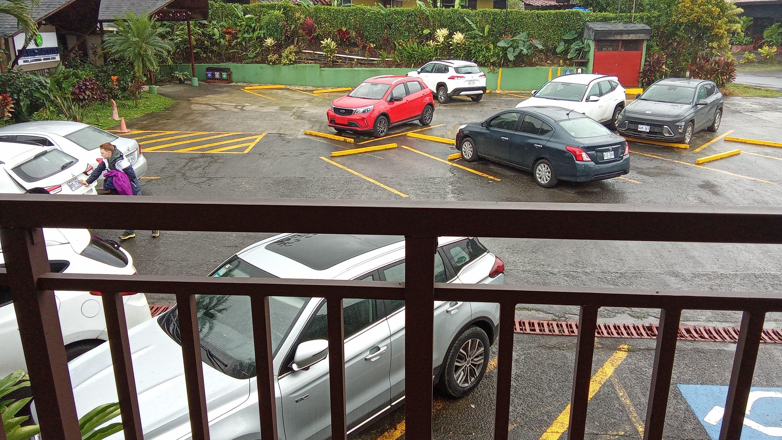 Um estacionamento com vários carros e uma pessoa perto de um carro branco.