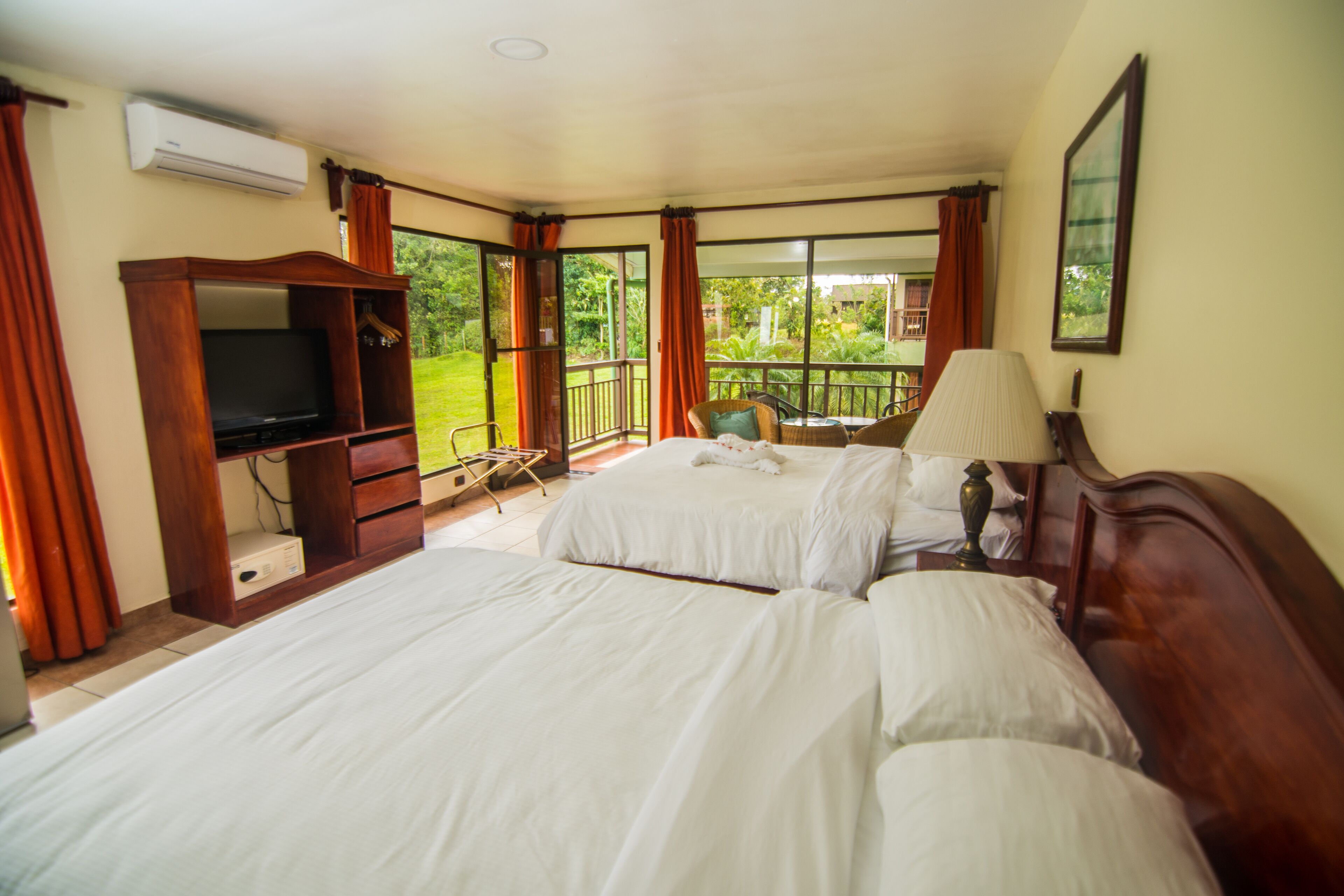 Een hotelkamer met twee bedden, een televisie, een balkon met een stoel en een groot raam.
