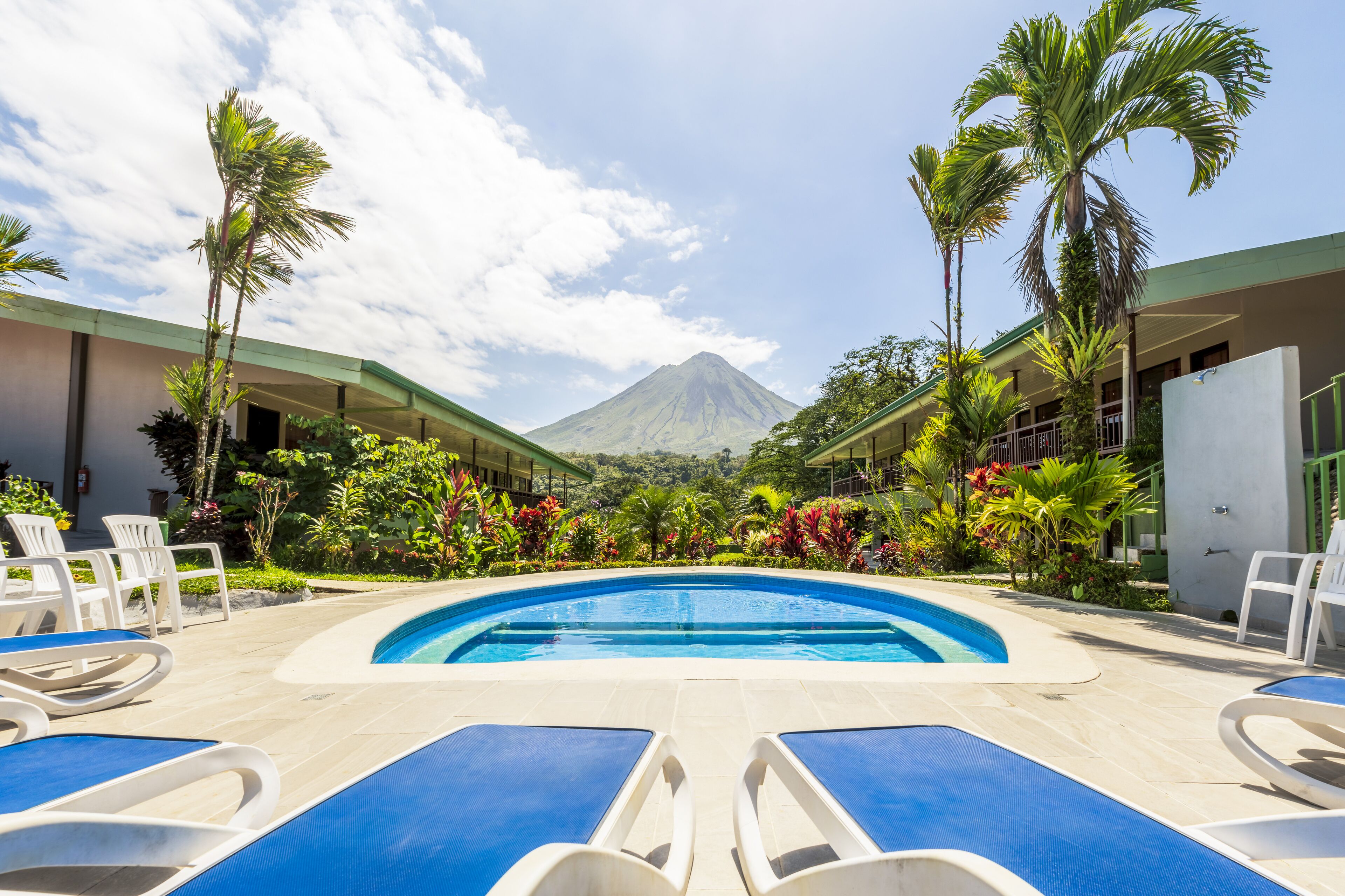 A swimming pool with lounge chairs, surrounded by palm trees and a mountain in the background.