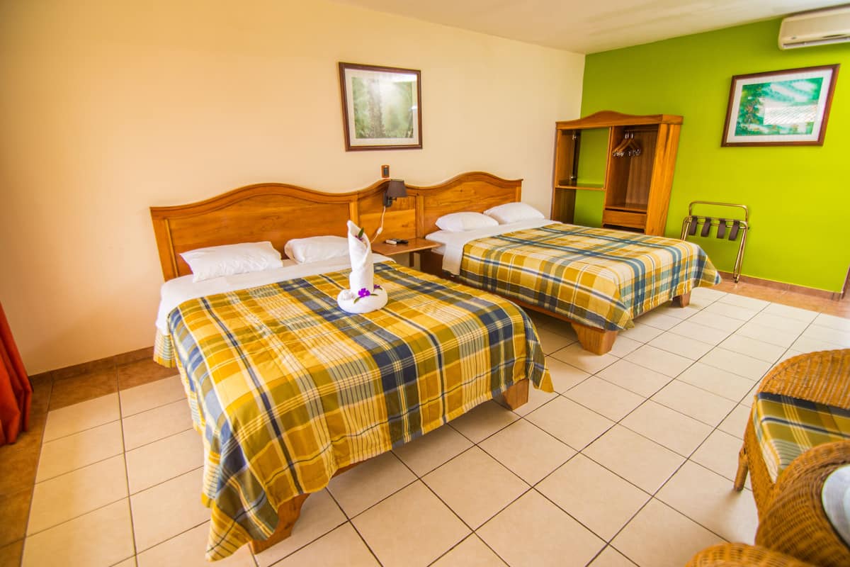 Een hotelkamer met twee bedden, een houten hoofdbord, een groene muur en een zithoek.