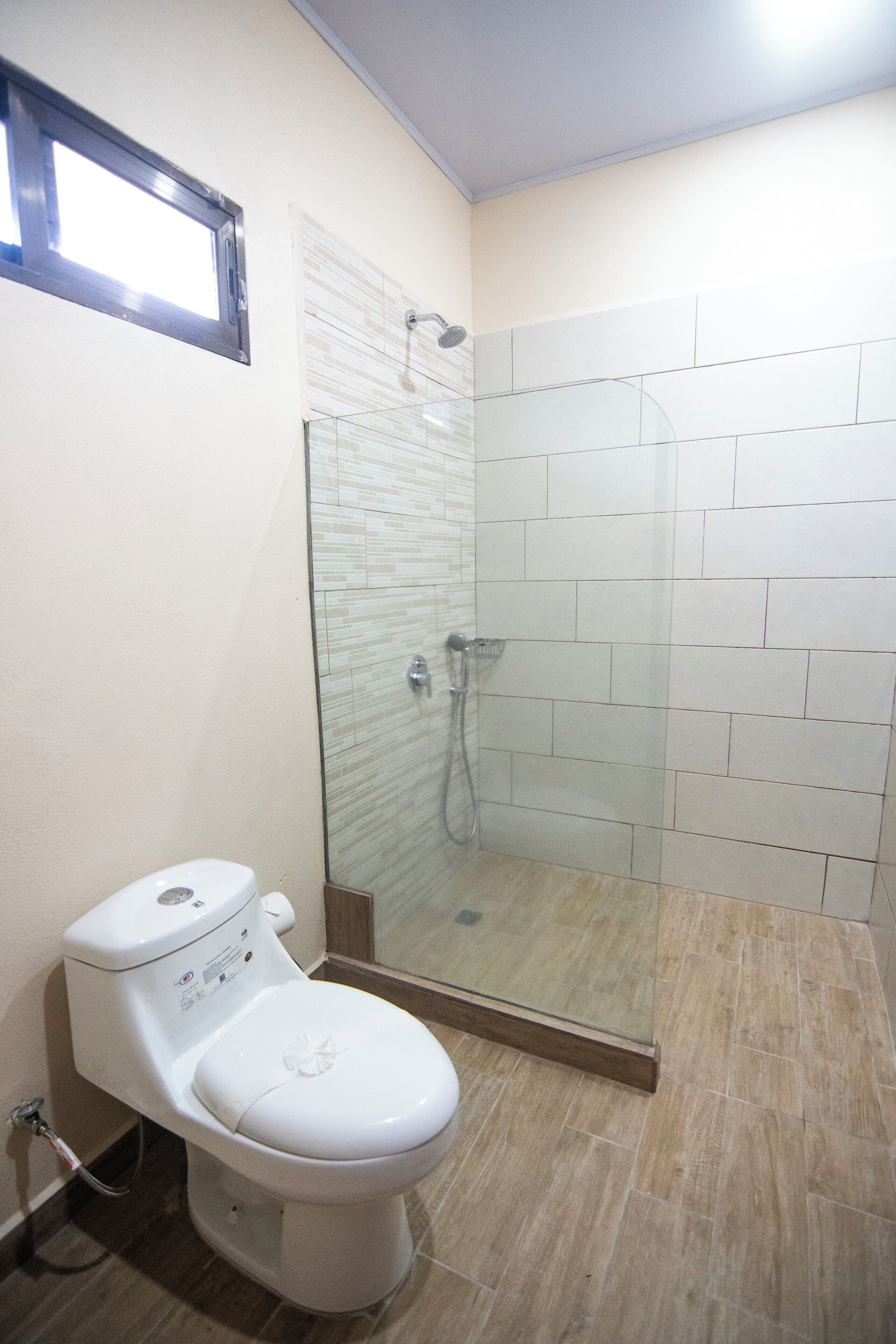 A bathroom with a toilet, a glass-enclosed shower, and tiled walls.