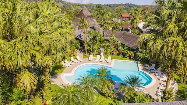 Un complexe hôtelier doté d’une grande piscine entourée de palmiers et de chaises longues.