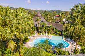 Een resort met een groot zwembad, omgeven door palmbomen en ligbedden.