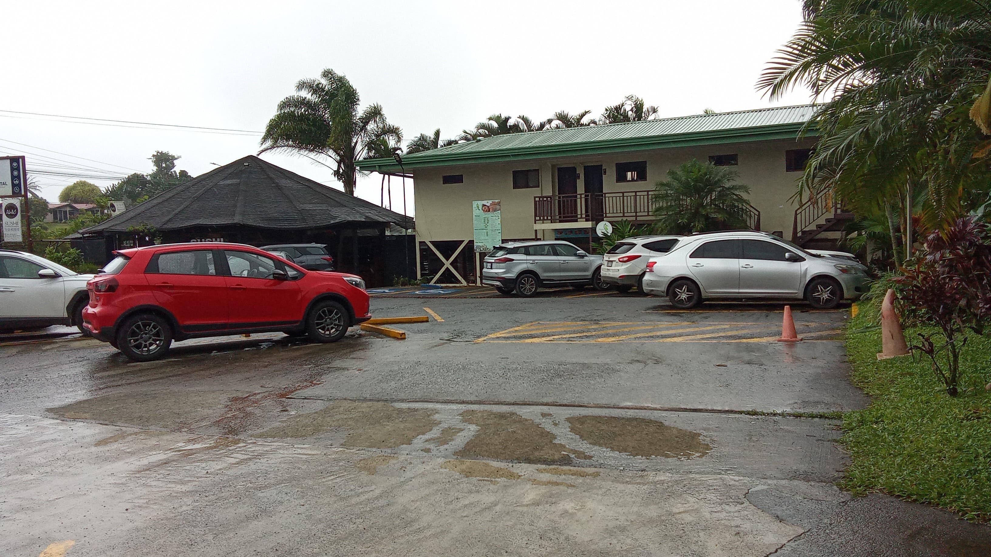 A parking area with cars, a building with a green roof, and a signboard.
