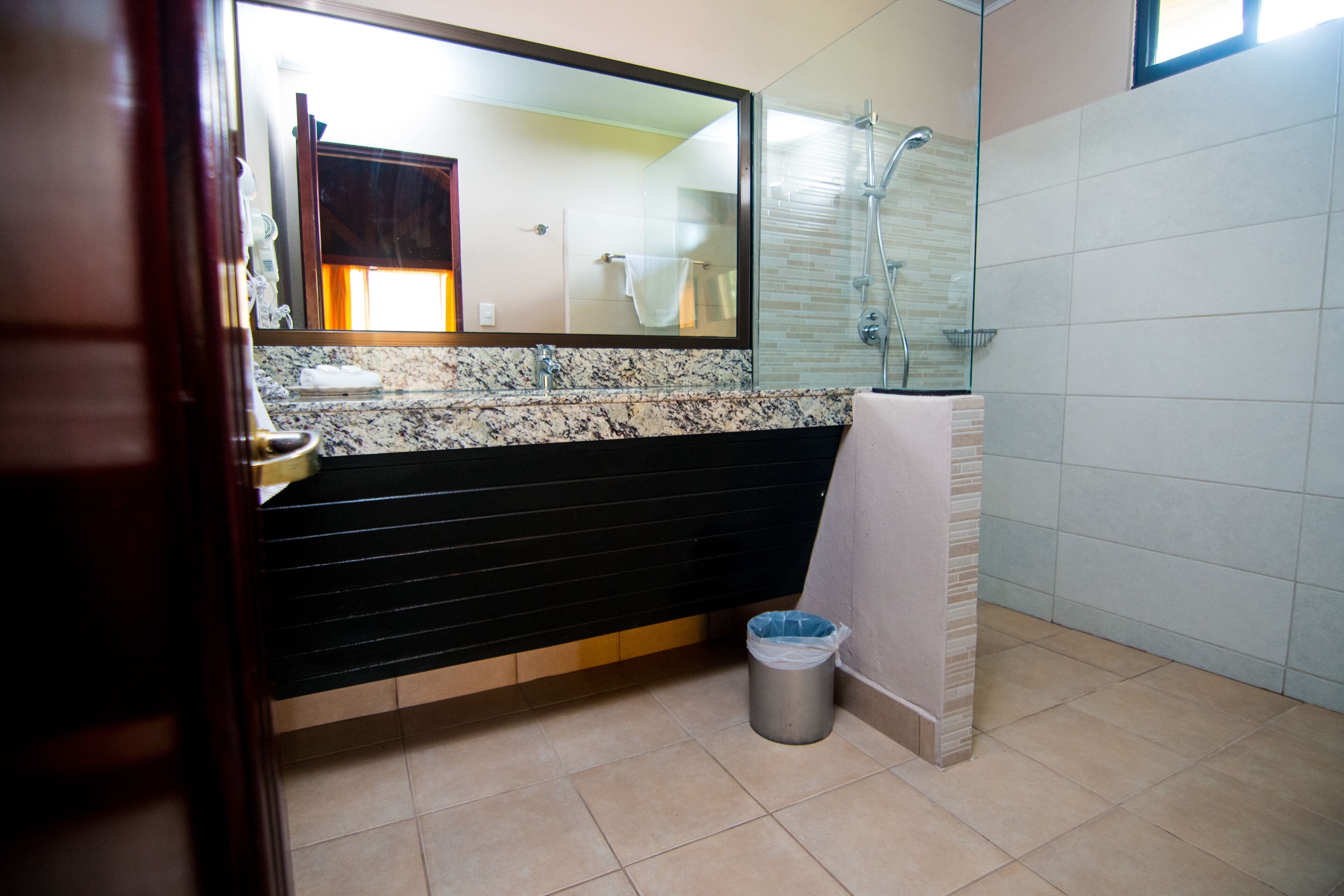 Un baño con lavamanos de mármol, tocador negro, cabina de ducha de vidrio y un cubo de basura.