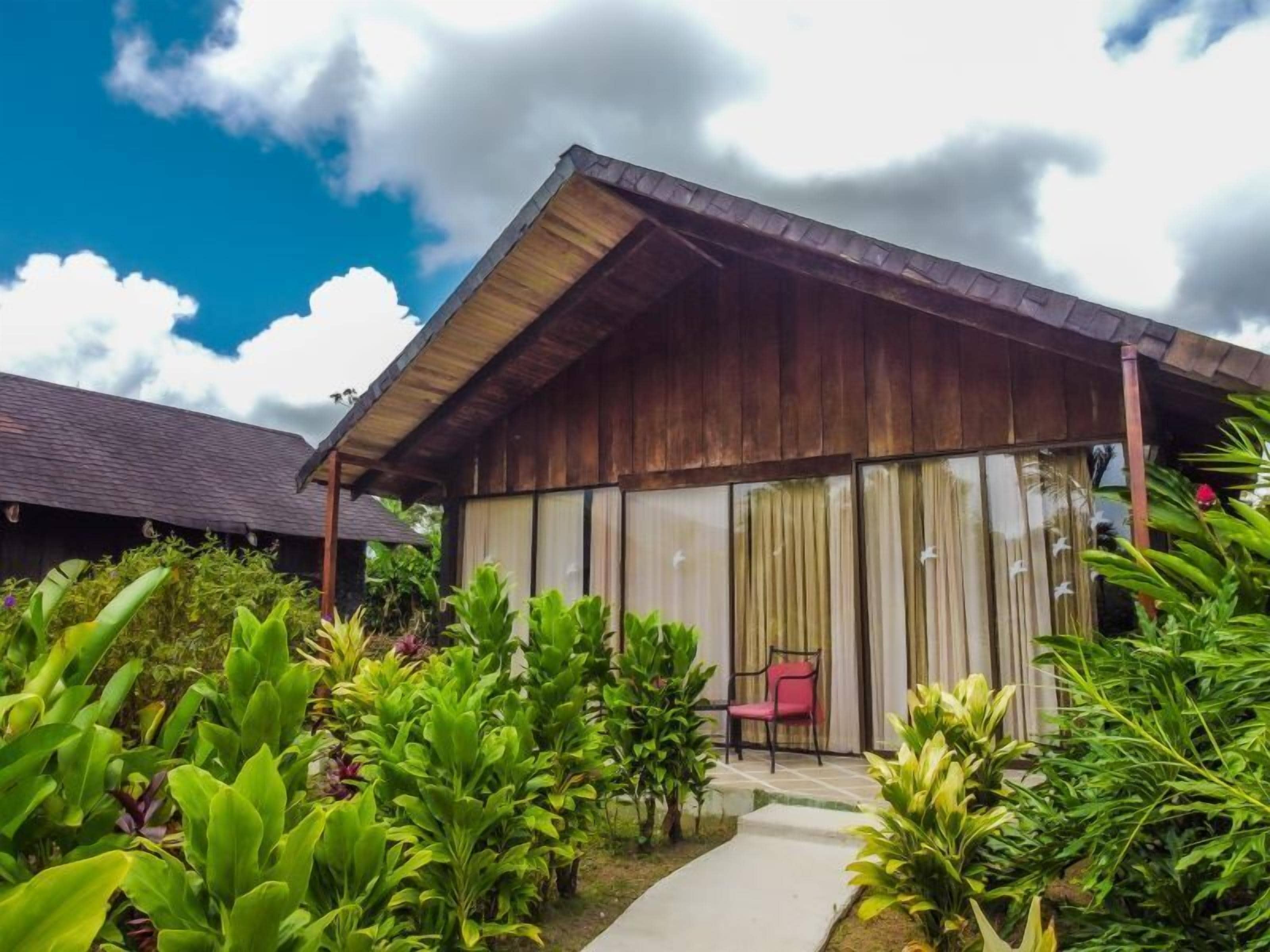 A wooden building with a covered patio area, surrounded by lush greenery.