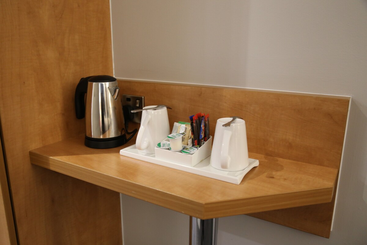 A wooden counter with a coffee maker, a kettle, and a tray with cups and pens.