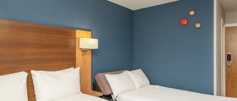 Habitación de hotel con dos camas, cabecero de madera, mesita de noche y lámpara de pared.