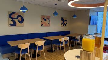 Un interno di un caffè moderno con sedute blu, tavoli in legno, opere d'arte astratte al muro e un angolo dedicato ai succhi di frutta.