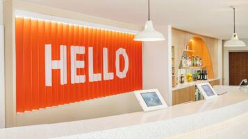 Ein Empfangsbereich mit einem großen 'HELLO'-Schild, einer Theke mit digitaler Anzeige und einer Bar mit Flaschen.