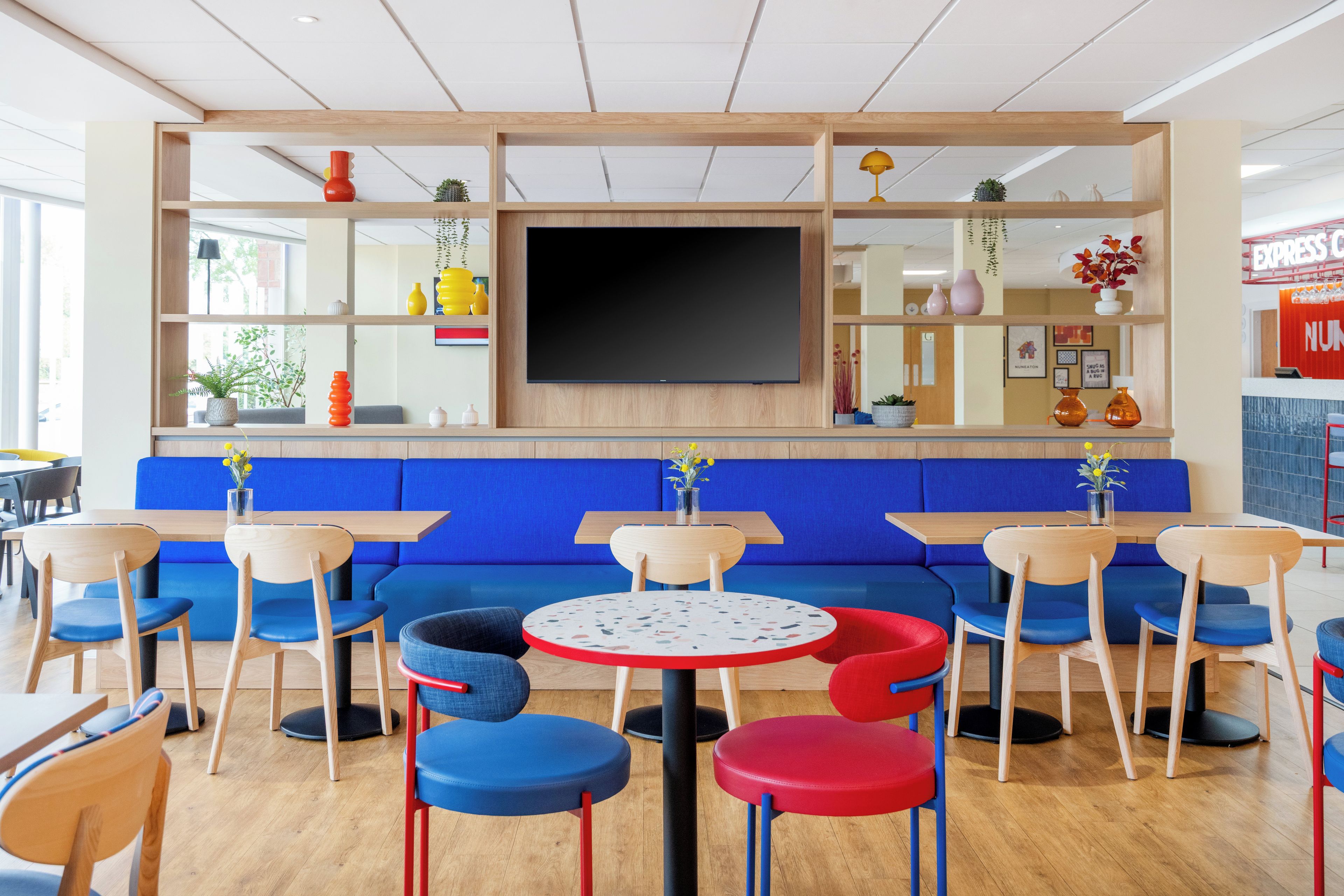 A modern interior with blue seating, wooden tables, and a flat-screen TV on the wall.