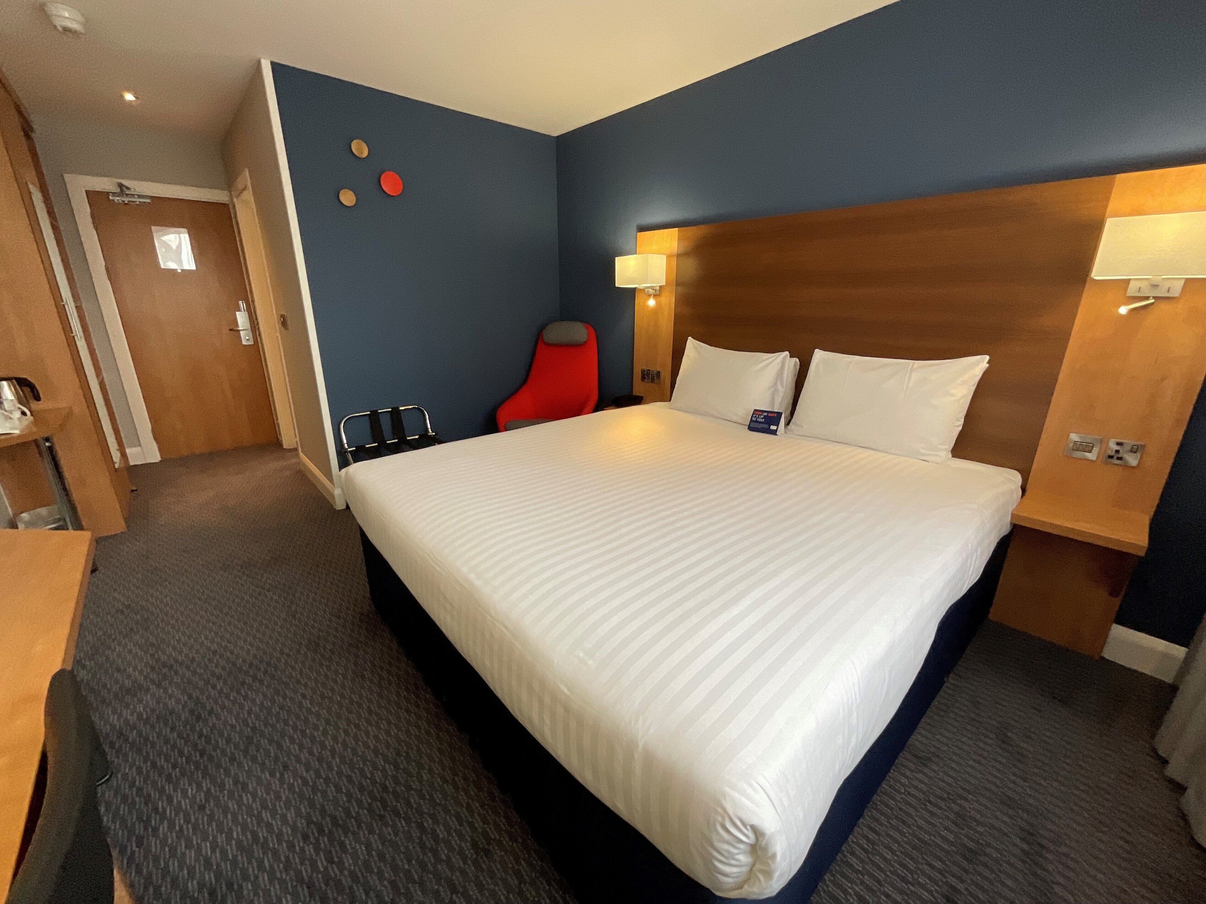 A hotel room with a large bed, a wooden headboard, a red chair, and a small table.