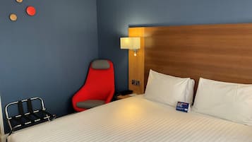 Ett hotellrum med en säng, en röd stol, ett sängbord och en vägglampa.