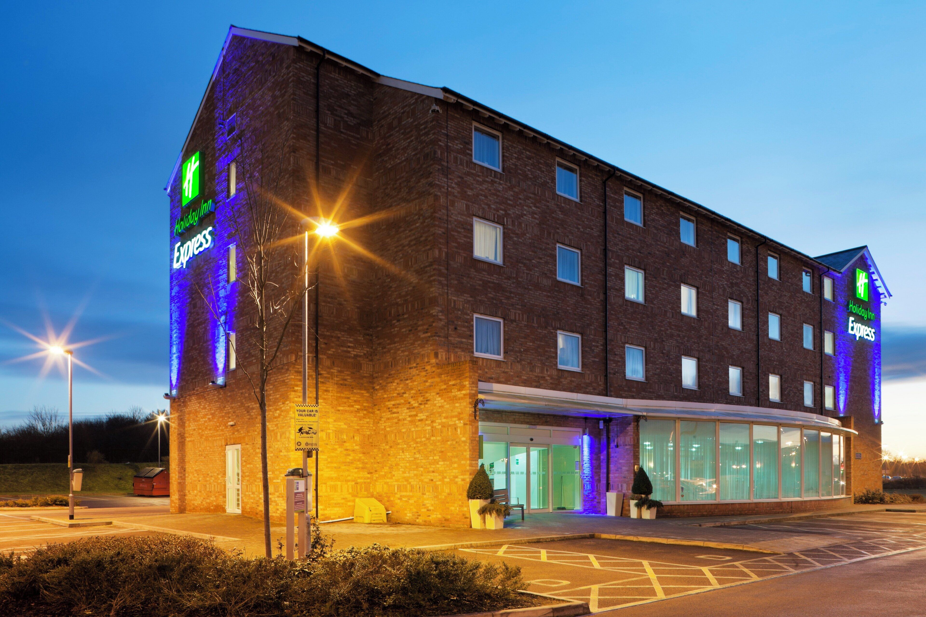 Un hotel Holiday Inn Express con fachada de ladrillo, amplias ventanas y estacionamiento.