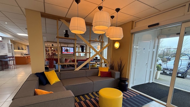 A modern lobby with a grey sofa, yellow ottoman, and a TV mounted on the wall.