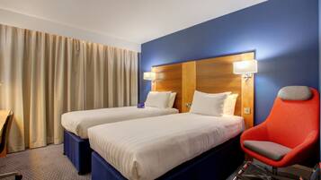 A hotel room with two beds, a red armchair, and a desk.