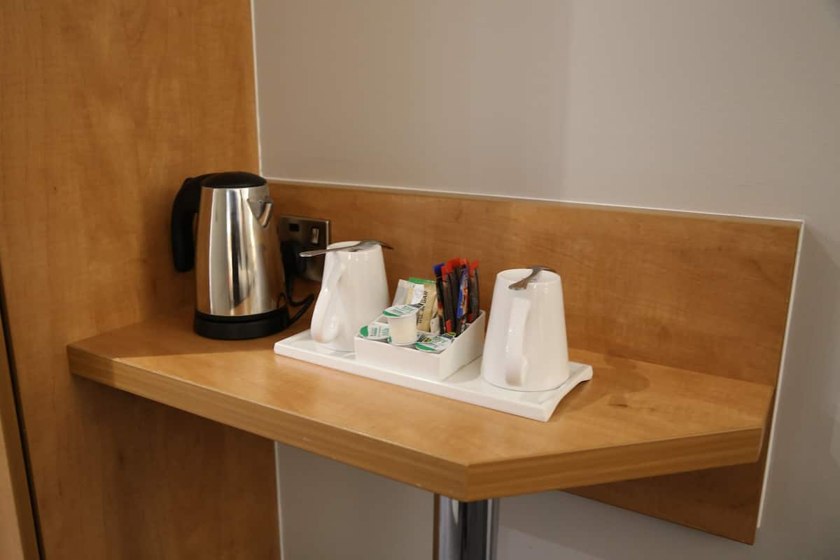 A wooden counter with a coffee maker, a kettle, and a tray with cups and pens.
