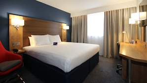 A hotel room with a large bed, a desk, a chair, and a mirror.