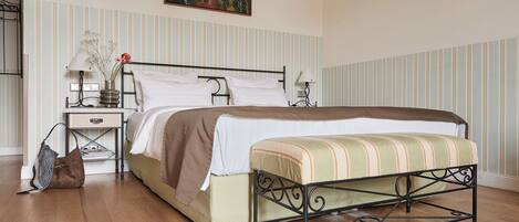 A bedroom with a bed, bedside tables, a lamp, a painting on the wall, and a wooden floor.