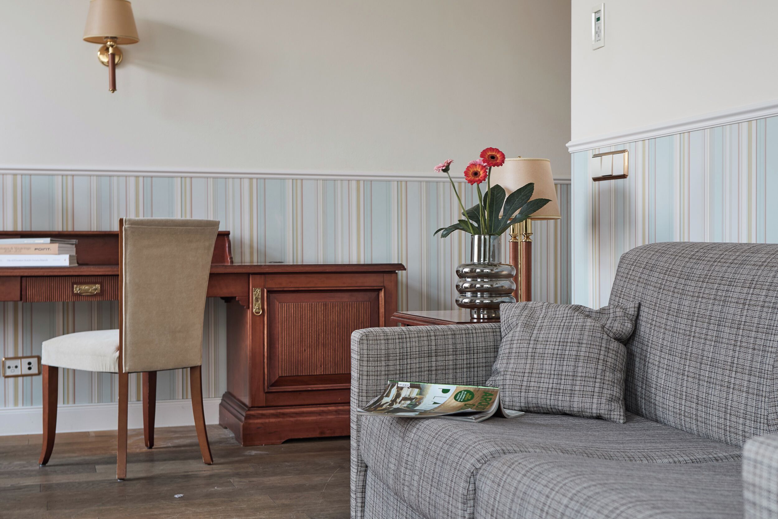 Ein Zimmer mit einem karierten Sofa, einem Holztisch, einem Stuhl, einer Lampe und einer Vase mit Blumen.