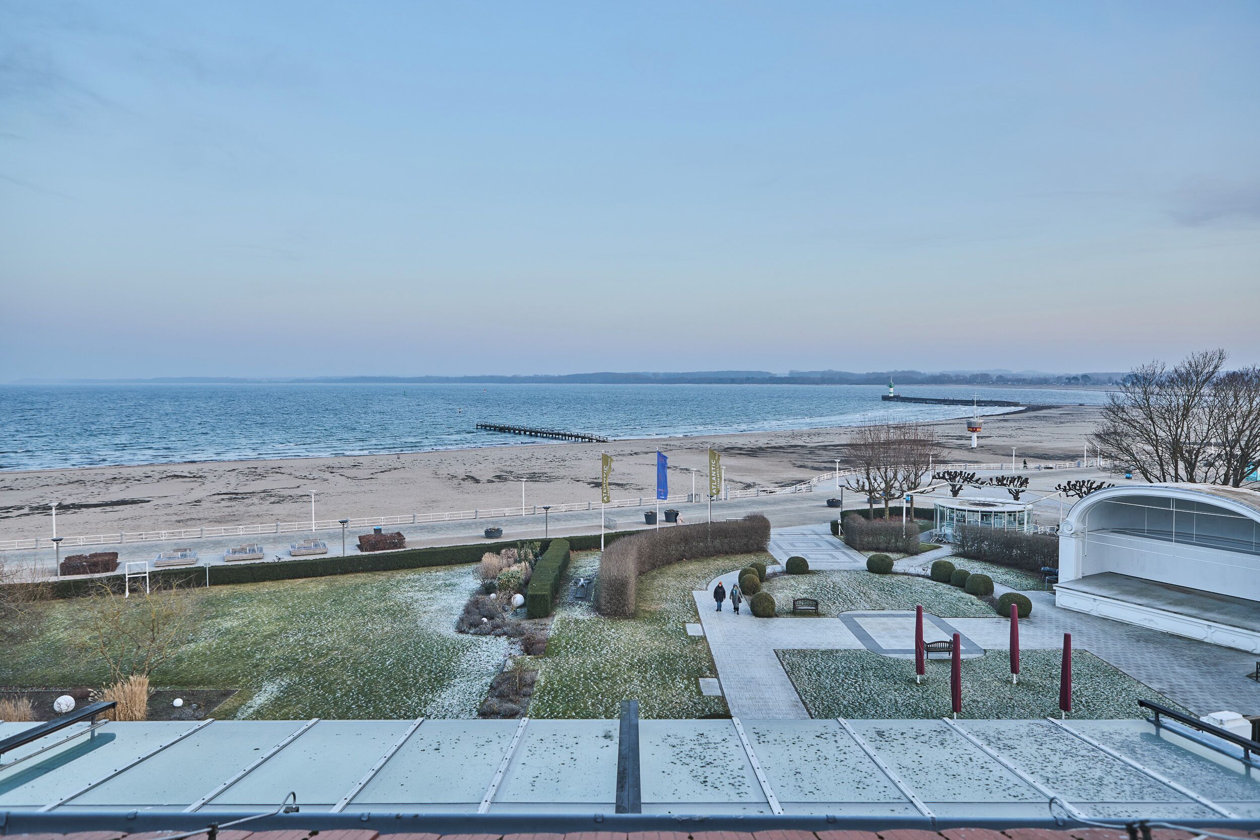 A coastal view with a promenade, a pier, and a modern building with a curved roof.