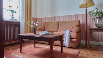 Ein Zimmer mit einem Holztisch, einem gestreiften Sofa, einer Lampe und einer Vase mit Blumen.