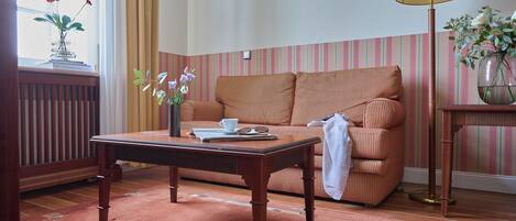 Una habitación con una mesa de madera, un sofá a rayas, una lámpara y un florero con flores.