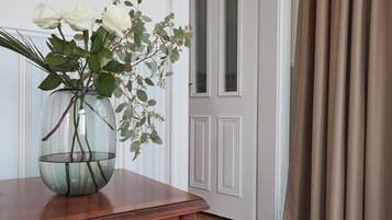 Vista despejada de una habitación con una mesa de madera, un jarrón de vidrio con flores blancas y una puerta con cortinas.