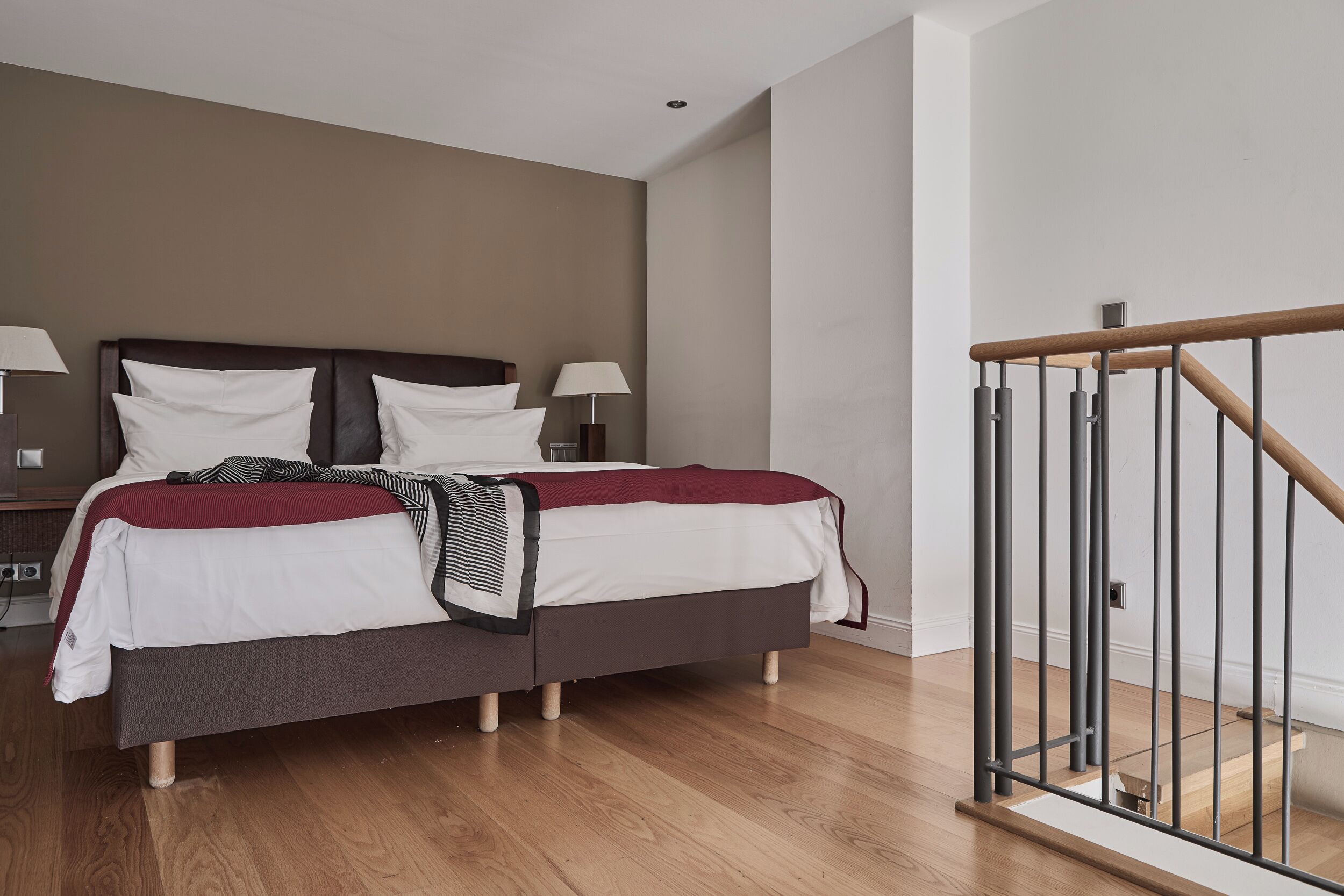 Ein Schlafzimmer mit einem Bett, Nachttischen, einer Lampe, Holzboden und einer Treppe mit Geländer.