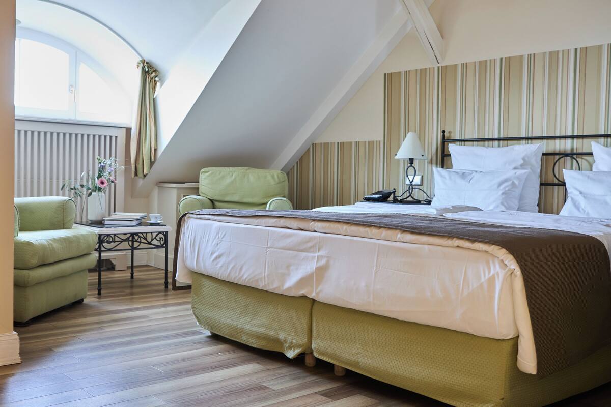 Habitación de hotel con cama, una silla, una mesa y ventana con cortinas.